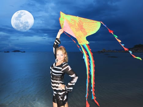 Beautiful woman with kite on the beach under moon