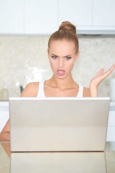 Woman seated at a table looking at her laptop screen in consternation and horror