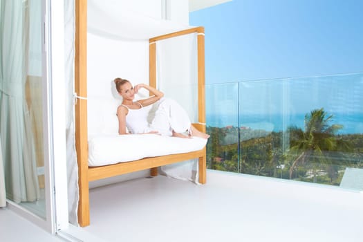 Woman relaxing on a canopied seat on a glass fronted patio overlooking the ocean enjoying tropical luxury