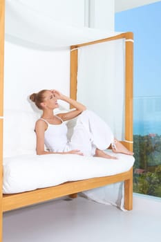 Woman relaxing on a canopied seat on a glass fronted patio overlooking the ocean enjoying tropical luxury