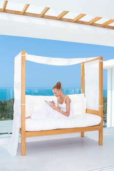 Fresh high key image of a beautiful woman wearing a white outfit relaxing on a white couch using a touchpad notebook