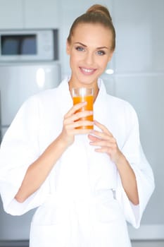 Beautiful elegant woman in a white bath robe drinking a large glass of fresh orange juice