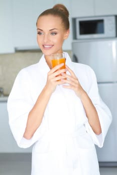 Stylish woman in a thick white towelling gown drinking a large glass of healthy orange juice