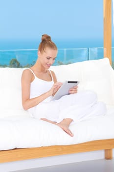 Fresh high key image of a beautiful woman wearing a white outfit relaxing on a white couch using a touchpad notebook