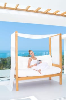 Fresh high key image of a beautiful woman wearing a white outfit relaxing on a white couch using a touchpad notebook