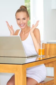 Healthy happy woman with a large glass of fresh orange juice seated at a table using her laptop