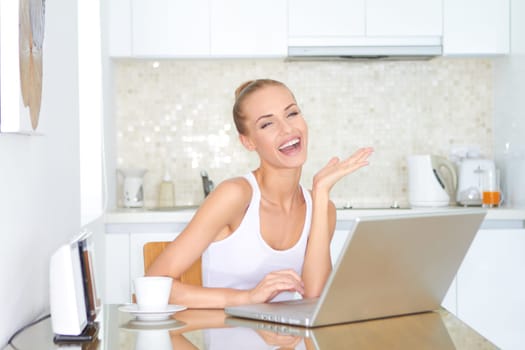 Laughing woman sitting at her laptop computer in her kitchen enjoying something she has just read over the internet