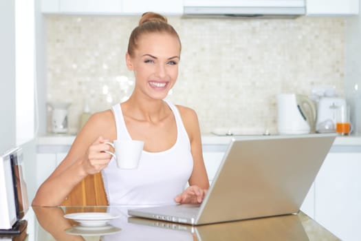 Laughing woman sitting at her laptop computer in her kitchen enjoying something she has just read over the internet