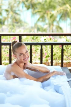 Beautiful elegant blonde woman sitting relaxing in an open-air tropical bubble bath