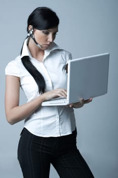Beautiful brunette business woman with wireless headset and laptop computer isolated on clear background