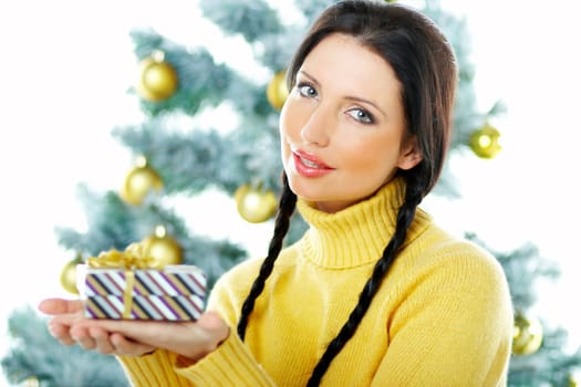 Beautiful brunette woman next to christmas tree on white background holding boxed gift