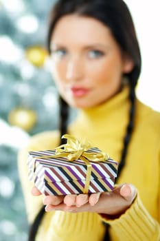 Beautiful brunette woman next to christmas tree on white background holding boxed gift