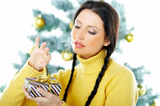 Beautiful brunette woman next to christmas tree on white background holding boxed gift