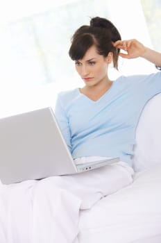 Young woman is on couch and working on laptop