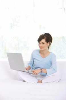 Young woman is on couch and working on laptop