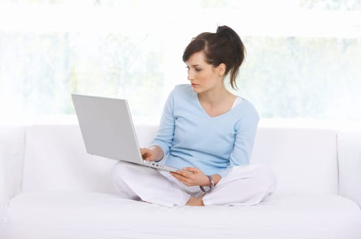 Young woman is on couch and working on laptop