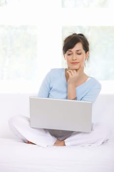 Young woman is on couch and working on laptop