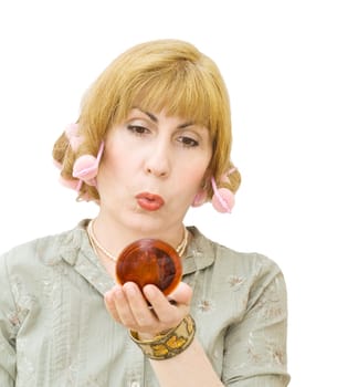 Housewife putting makeups, getting ready to go party, wearing hair rollers and looking into the mirror. Isolated over white background.