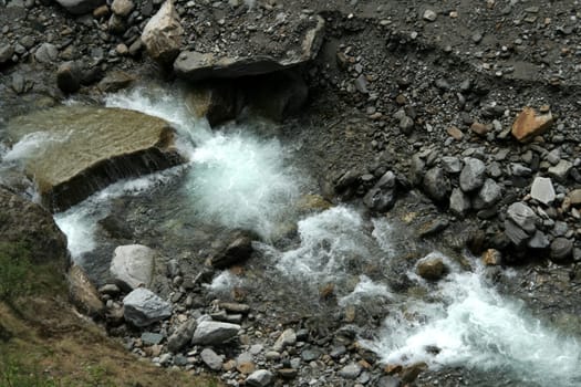 Pattern of spray of water flowing between stones and over pebbles