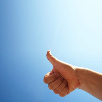 Male hand showing thumbs up in blue sky