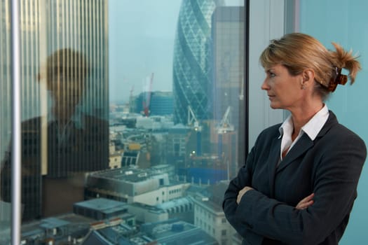 Senior business woman looking out of window with city of London in background