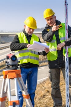 Land surveyors on highway reading geodesist plans use tacheometer