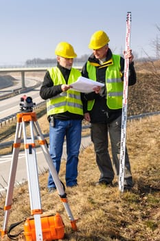 Land surveyors on highway reading geodesist plans use tacheometer