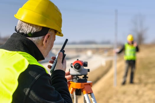 Land surveyors measuring with tacheometer speaking through transmitter highway