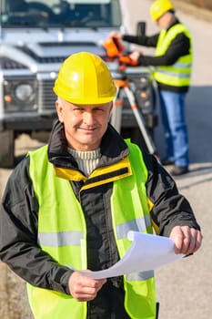Male geodesist in reflective vest and helmet hold land plans
