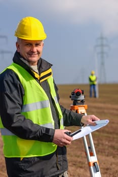 Land surveyors measuring with tacheometer hold construction plans on site