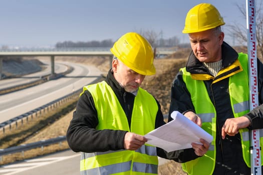 Land surveyors on highway reading geodesist plans use tacheometer
