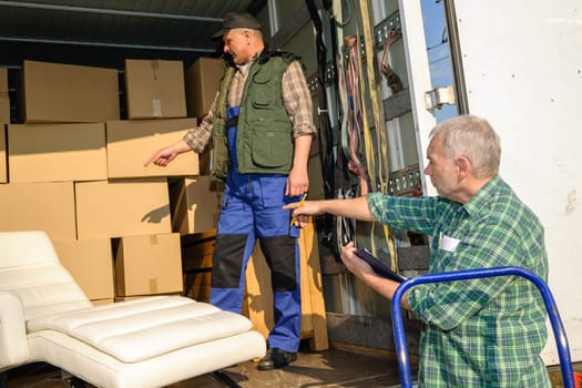 Two male movers unload furniture and boxes from moving truck