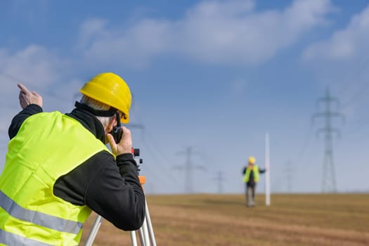 Land surveyors measuring with tacheometer speaking through transmitter construction site
