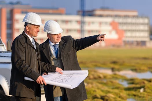 Two senior architect developers review plans at a construction site