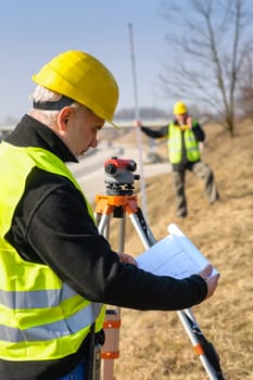 Land surveyors on highway reading geodesist plans use tacheometer