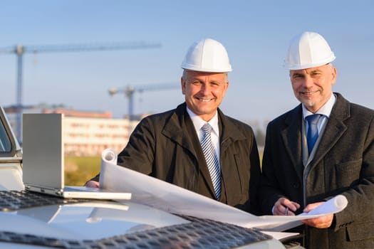 Male developers with blueprints at construction site discuss architect project