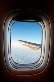 An airplane window with wing and cloudscape