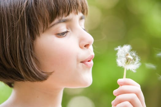 young girl blowing the seeds from a dandelion