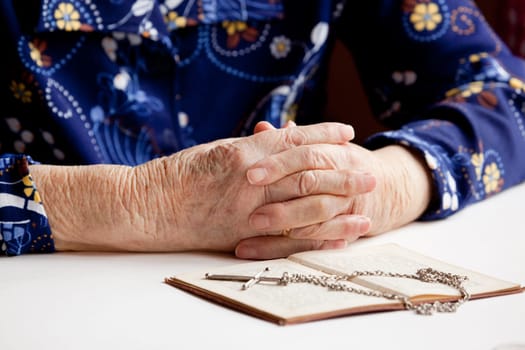 Old folded hands in front of a book and cross.  Focus on the hands.