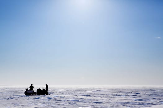 A barren flat winter landscape with two people and snowmobiles