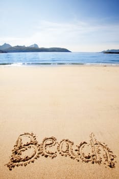 Beach written in the sand on the coast with mountains in the background