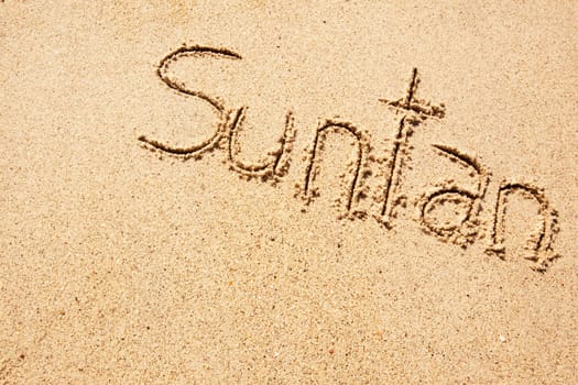 The word suntan written in the sand on a beach