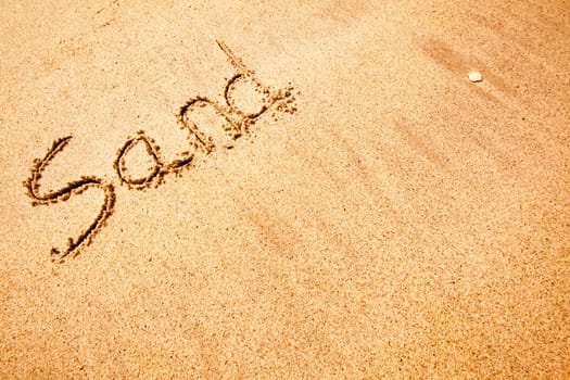 The word sand written in the sand at a beach - background texture