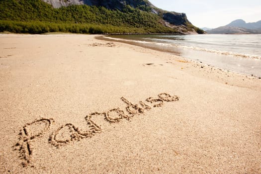 The word paradise written in the sand on a beautiful island