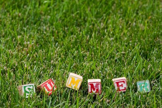 Wooden baby block spelling the word summer in grass