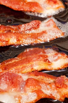 Bacon detail frying in a frying pan with grease