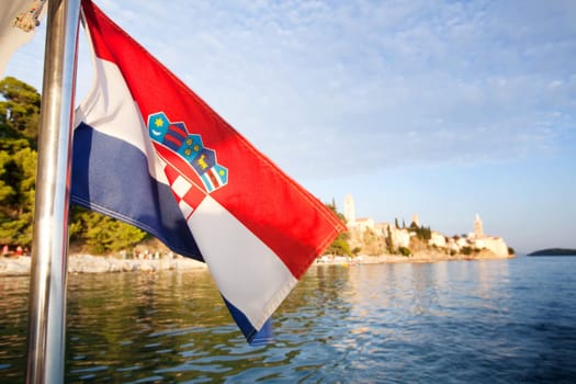 A croatian flag in front of a landscape of the island of Rab