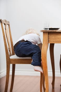 Cute blond child trying to get down from chair near dining table