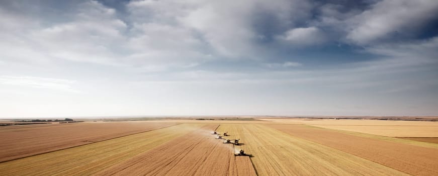 Panoramic landscape with four combines in a field on the open prairie