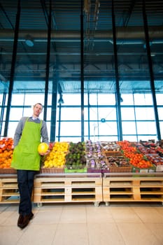 An owner of a grocery store standing by fruits and vegetables